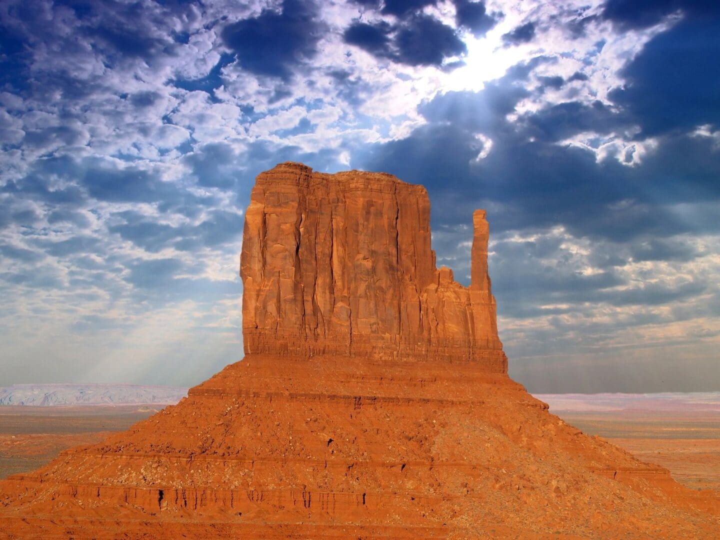 A monument valley rock formation with the sun shining in the background.