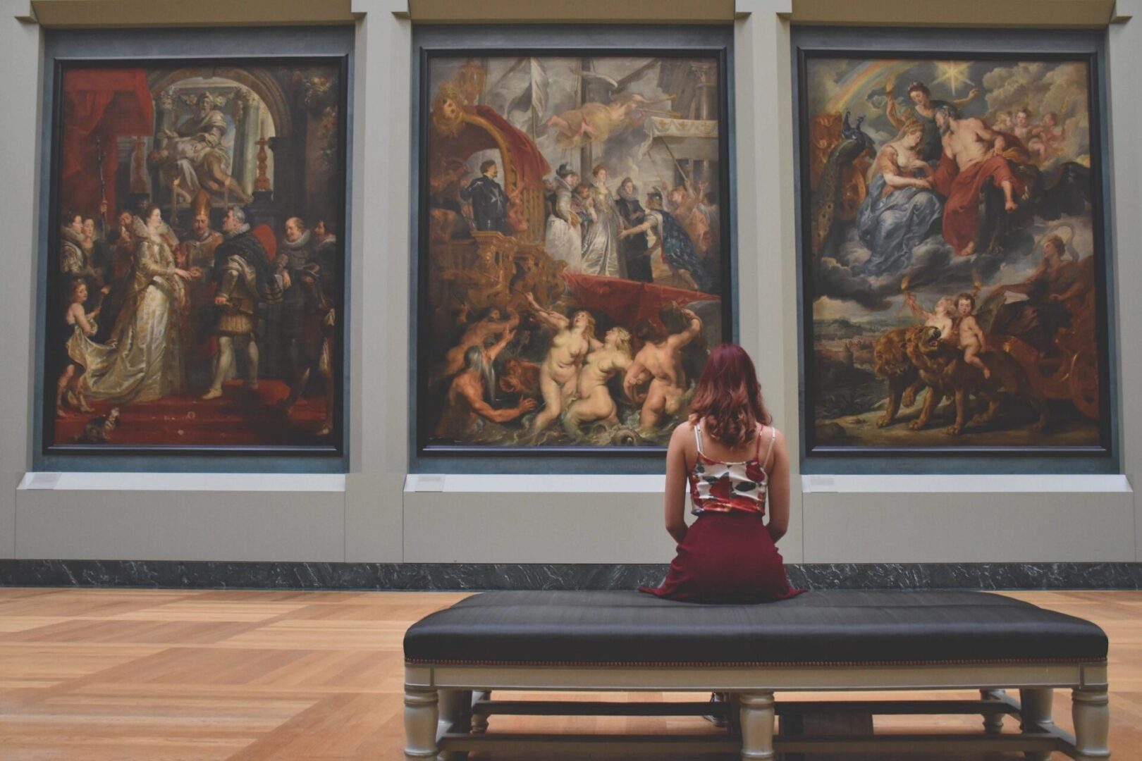 A woman sitting on top of a bench in front of paintings.